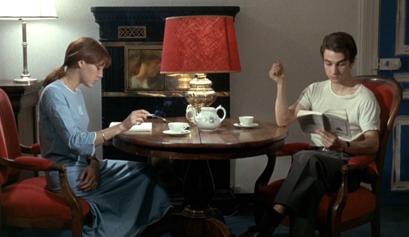 A still of Anne Wiazemsky and Jean-Pierre Leaud in Le Chinoise. They are sitting at a table reading and smoking cigarettes.