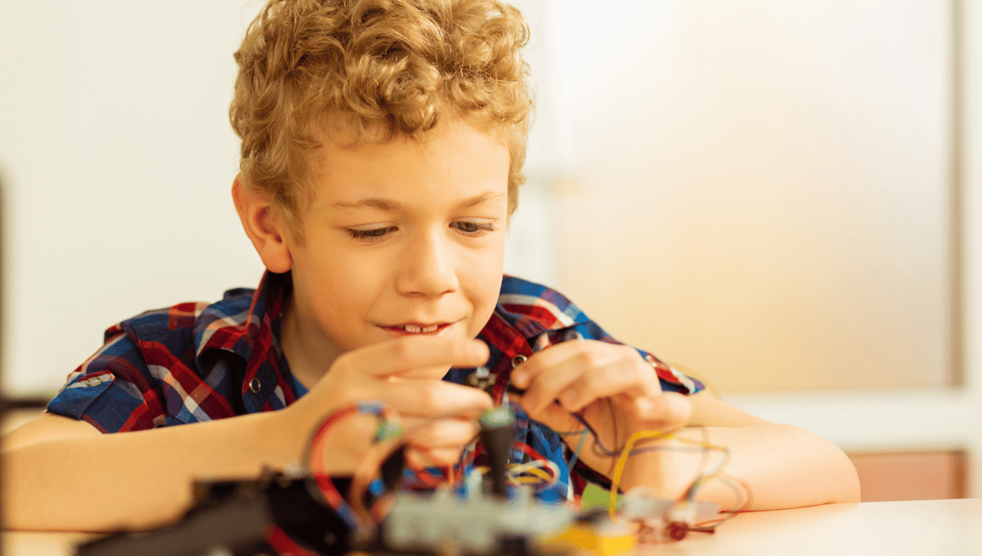 Child in a plaid shirt playing with some multicoloured wires.