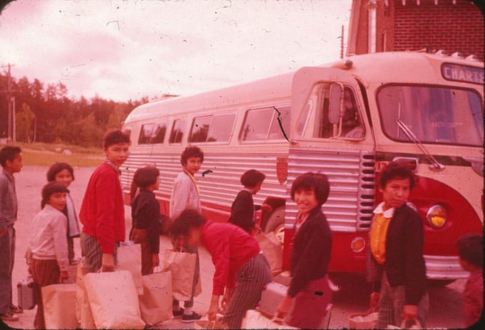 Students boarding a chartered bus, carrying suitcases and tote bags. 