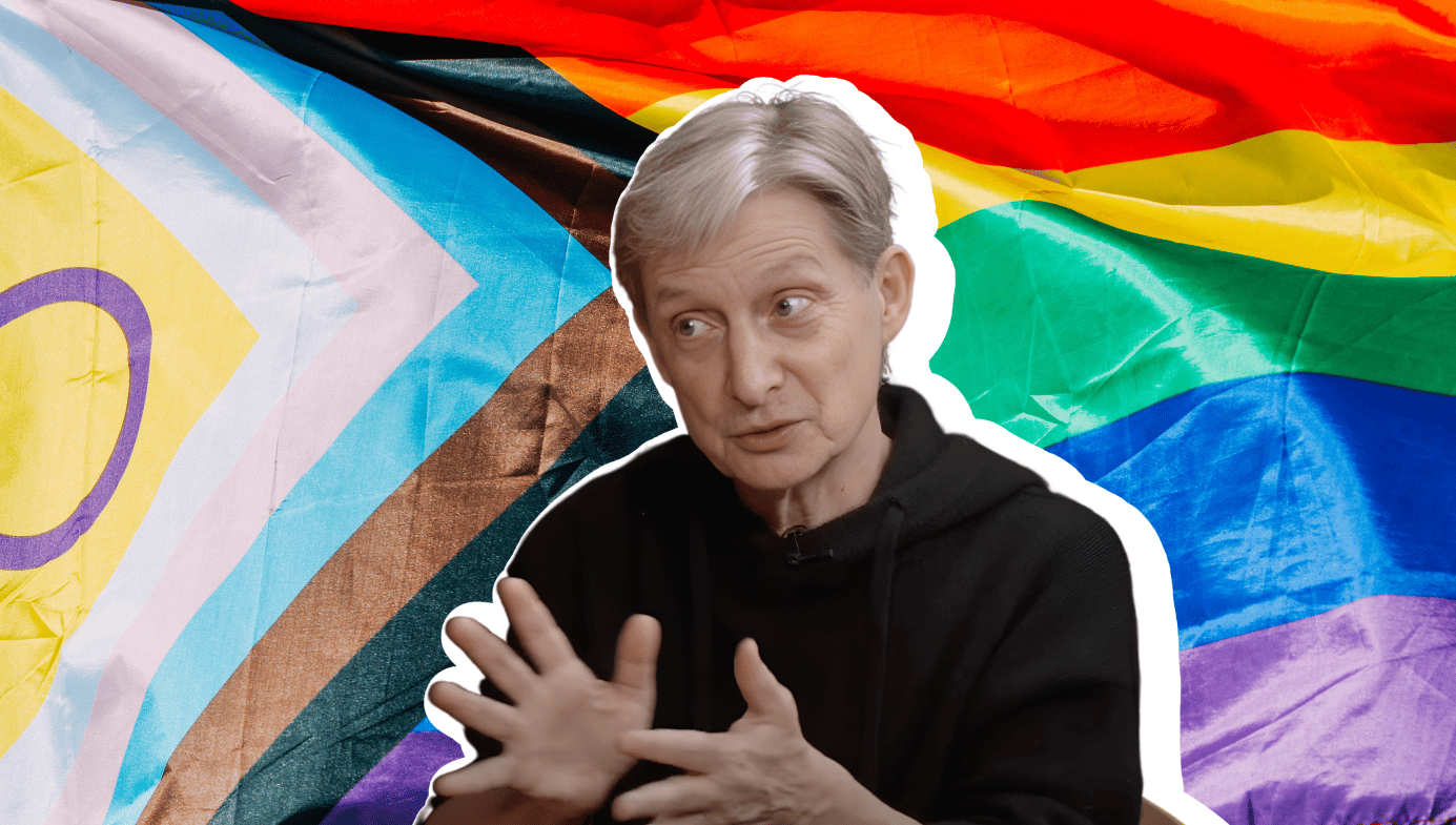 A still image of Judith Butler speaking. An LGBTIQ flag in the background. 