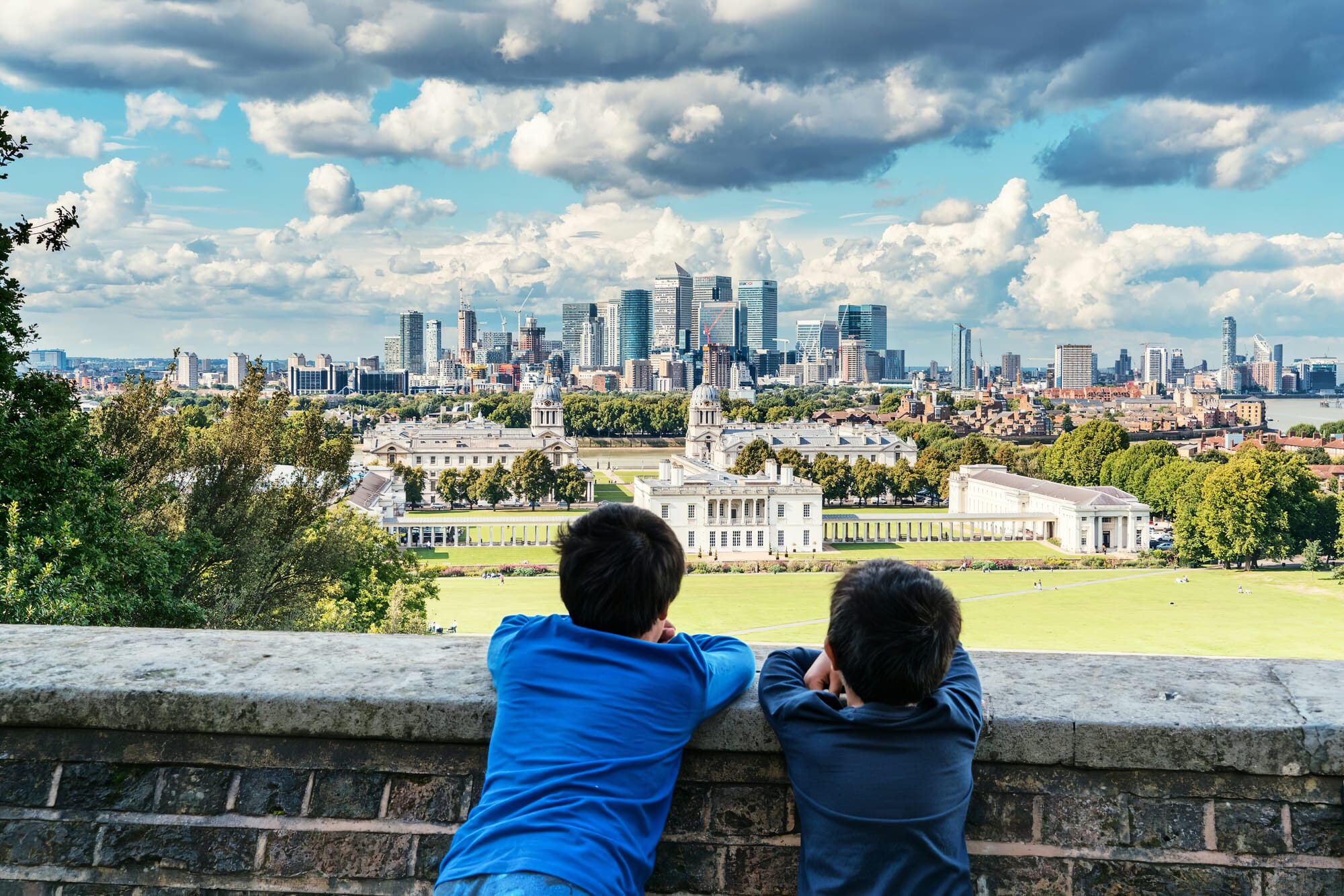 Two boys looking out at the skyline of Greenwich, London, from above.  