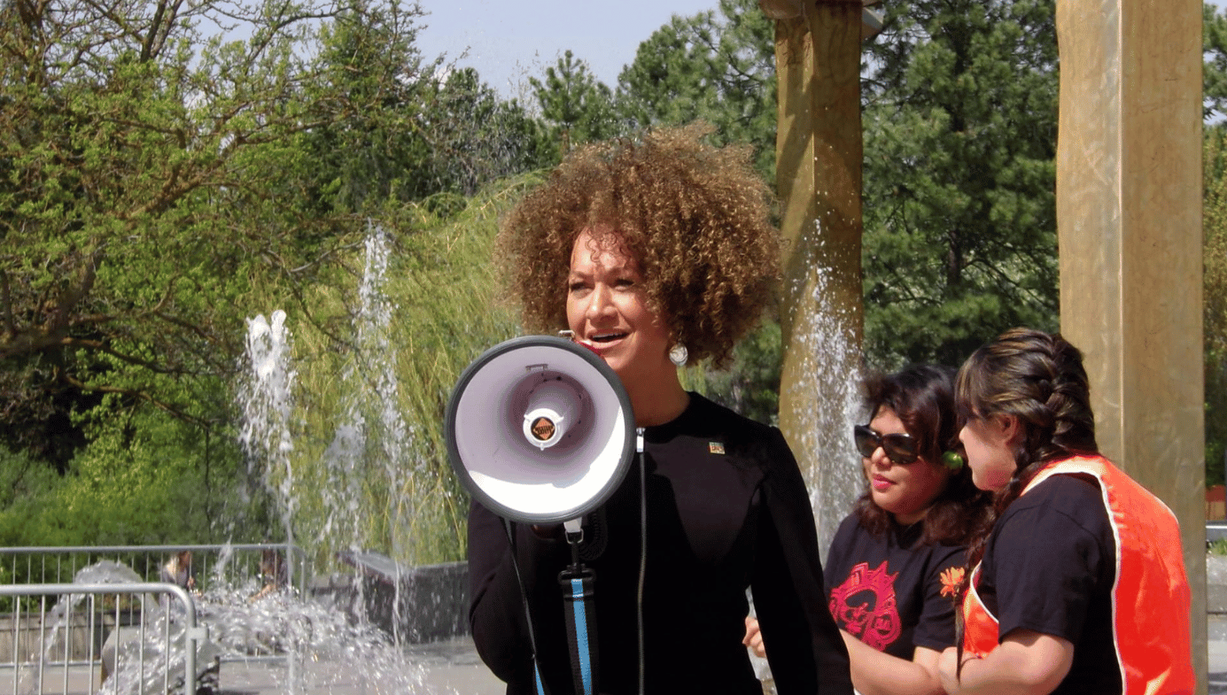 Rachel Dolezal with a loudspeaker, speaking at a rally in Spokane, Washington, in front of a fountain.