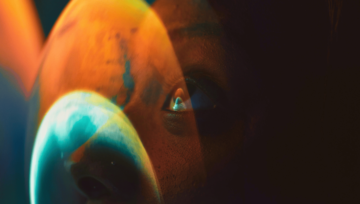 An abstract photo of a woman looking through an astronaut helmet with a reflection of planets in the glass.