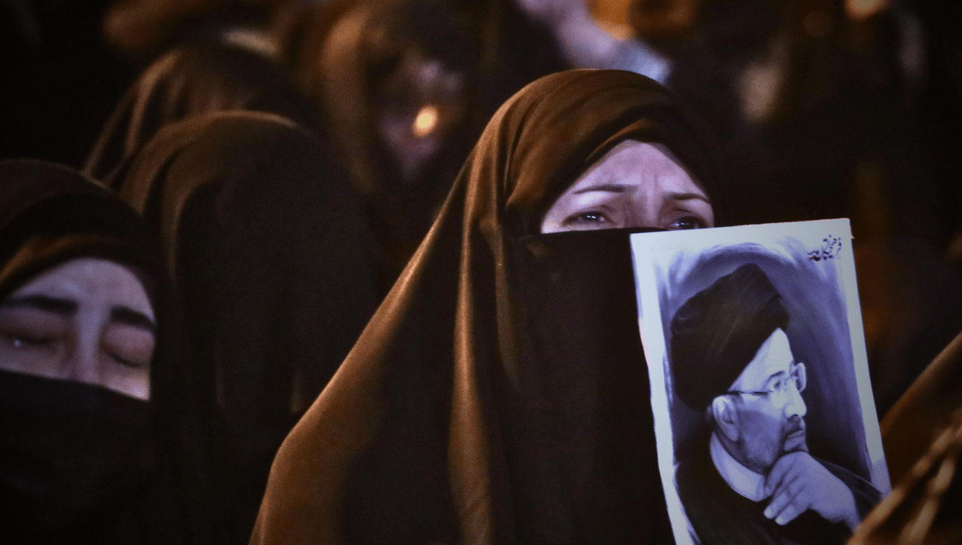 A crying woman in a black burqa at the commemoration of Raisi's death. She holds a poster of him.