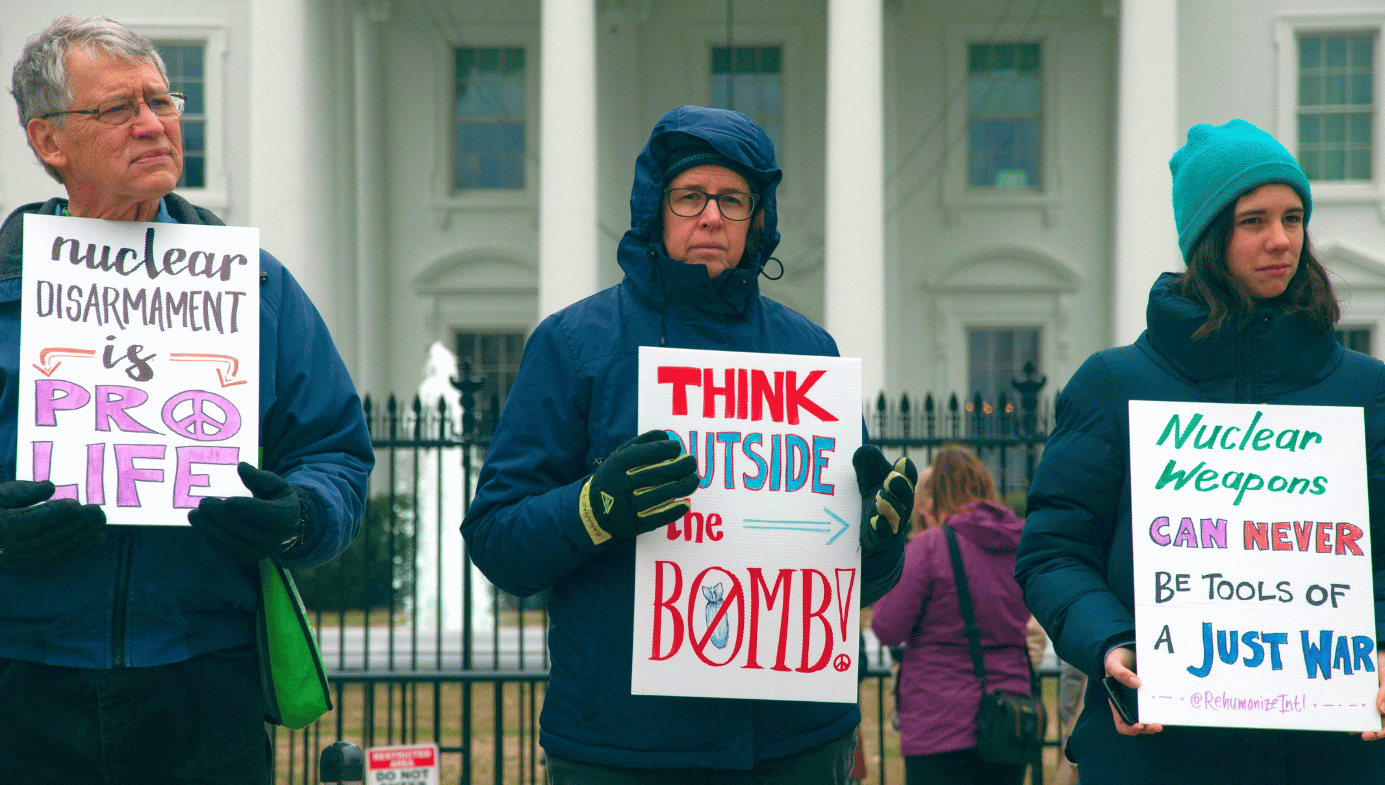 Three people holding nuclear disarmament protest signs in front of the White House.