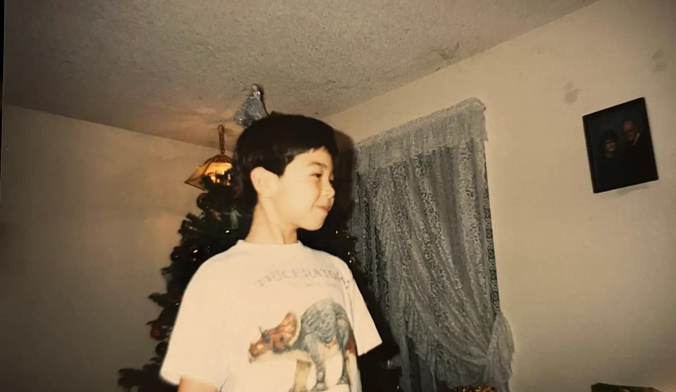 A childhood photo of Rob Henderson in a humble living room, smiling in front of a Christmas tree.