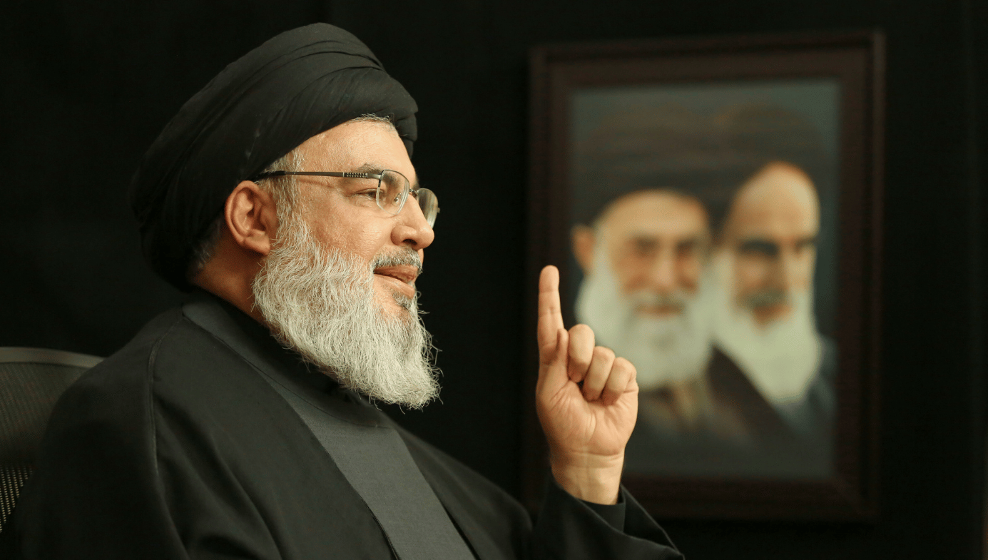 Hezbollah leader Sayyed Hassan Nasrallah, raising his finger with image of Khamenei and Khomeini in the background