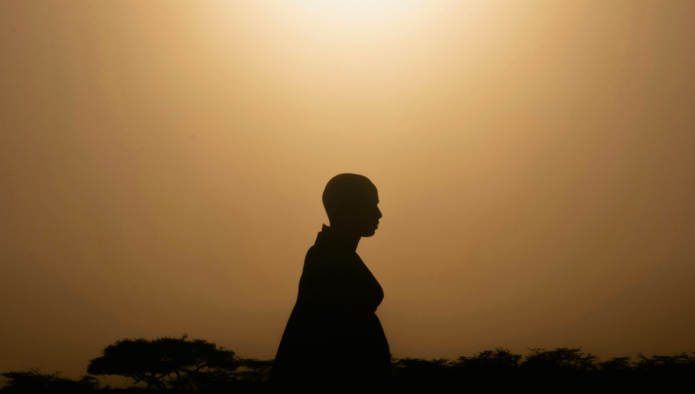 Masai man standing against sunrise from Masai Mara National Park, Kenya.