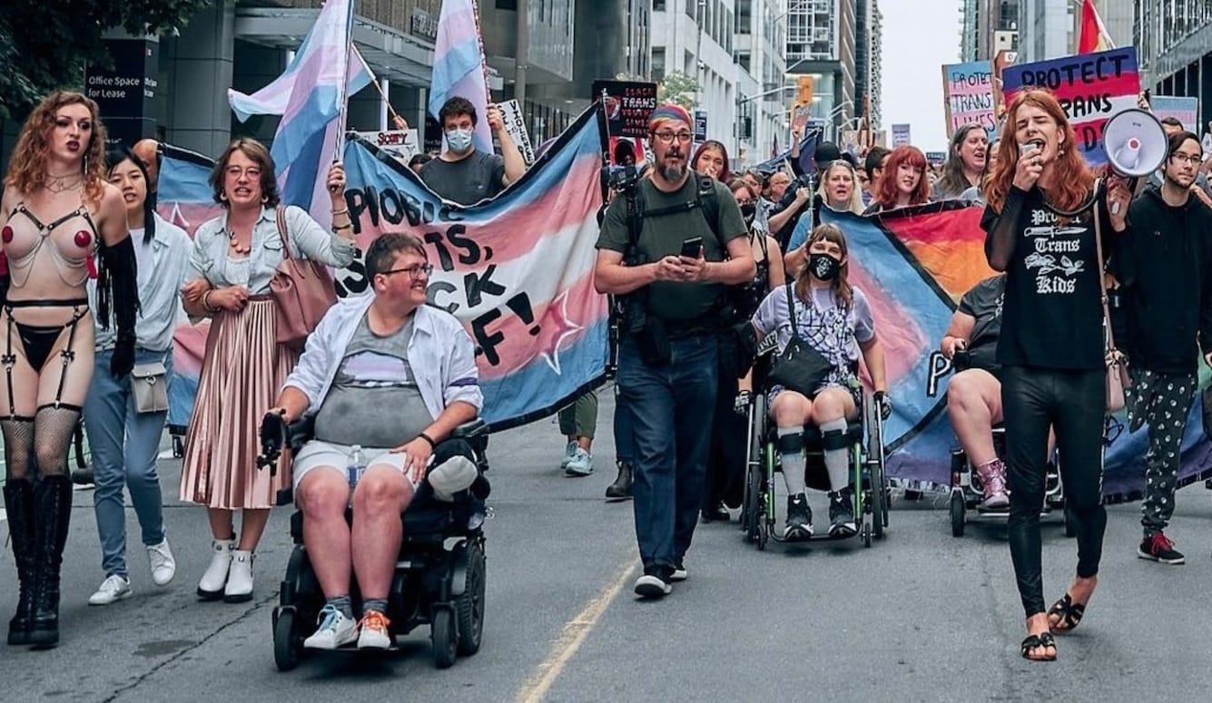 People on a trans-rights protest march, with flags, megaphone, banners. 