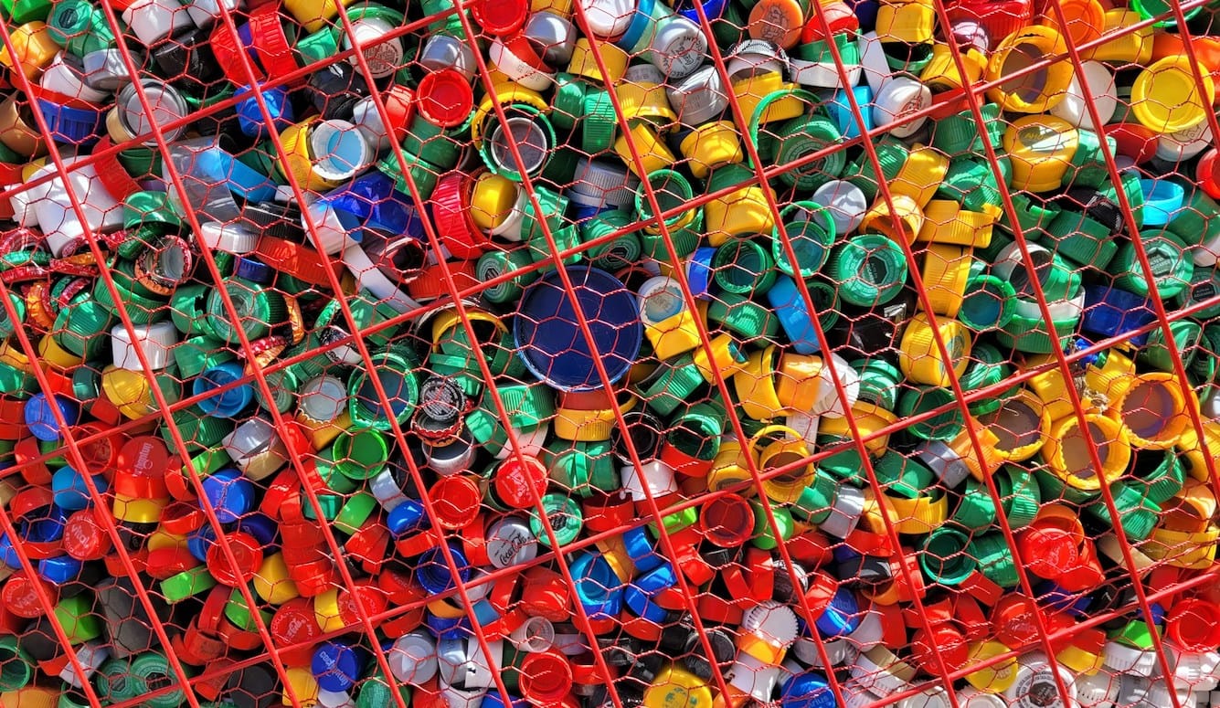 Colourful plastic bottle tops in a recycling bin.