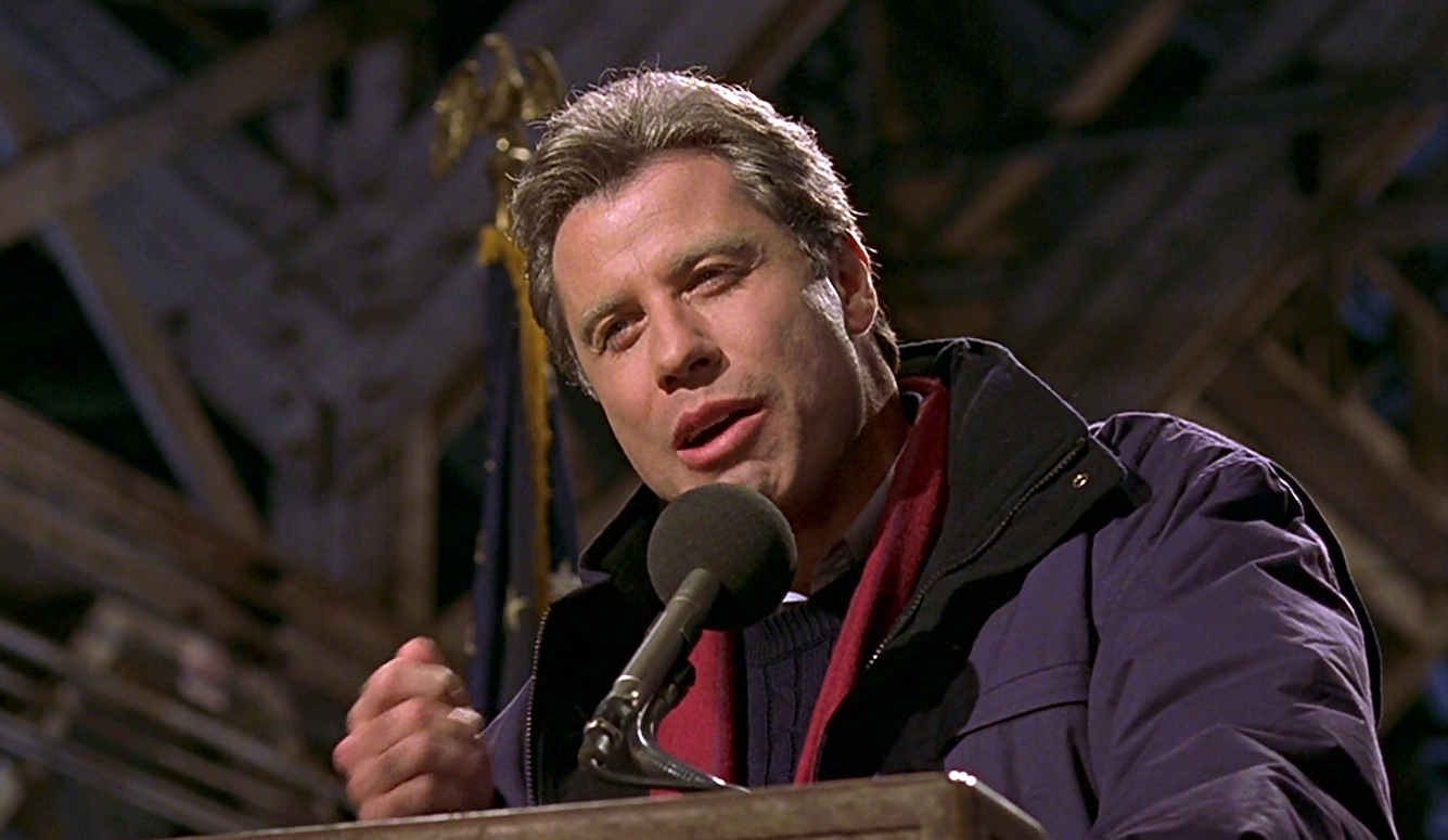 John Travolta at a lectern, speaking.