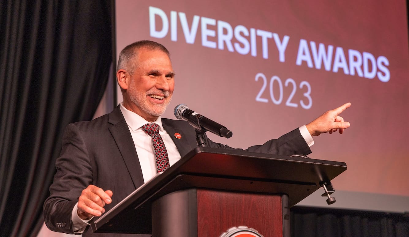 A man on a podium, in suit and tie, pointing to a slide that says "Diversity Awards 2023." 