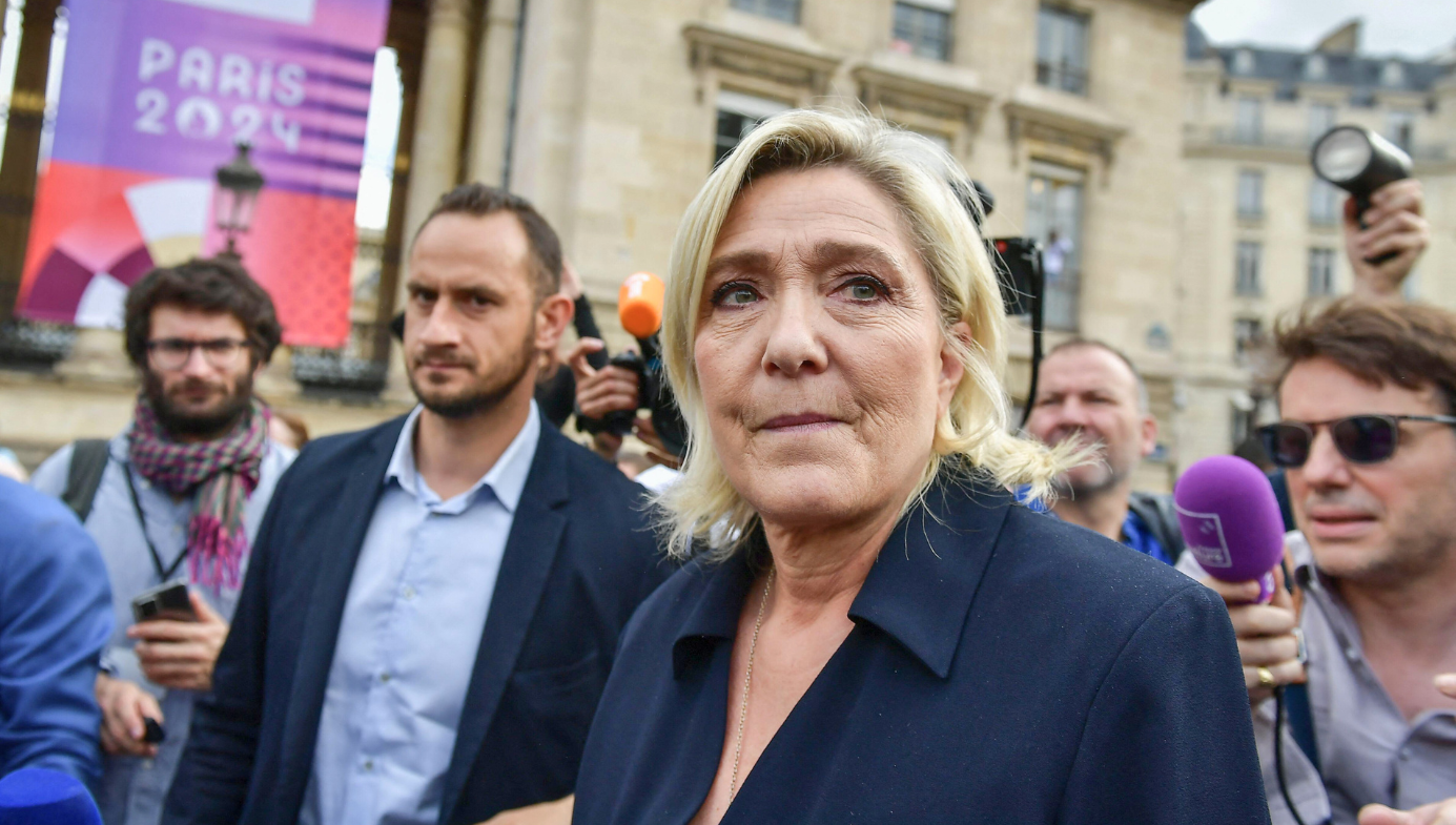 Marine Le Pen with a concerned look on her face surrounded by a crowd of press in Paris.