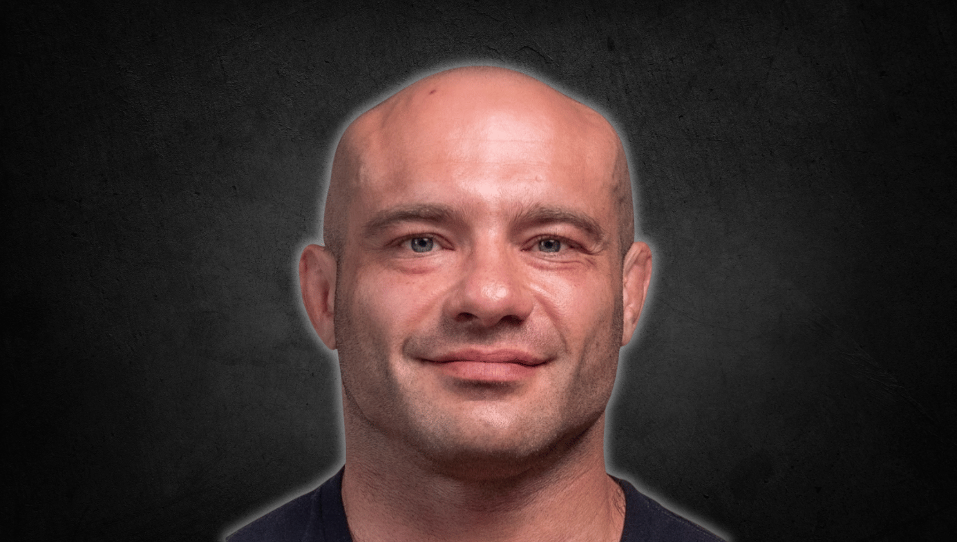 Head and shoulders photo of Mike Israetel, bald, stocky, smiling slightly, in a dark navy T-shirt