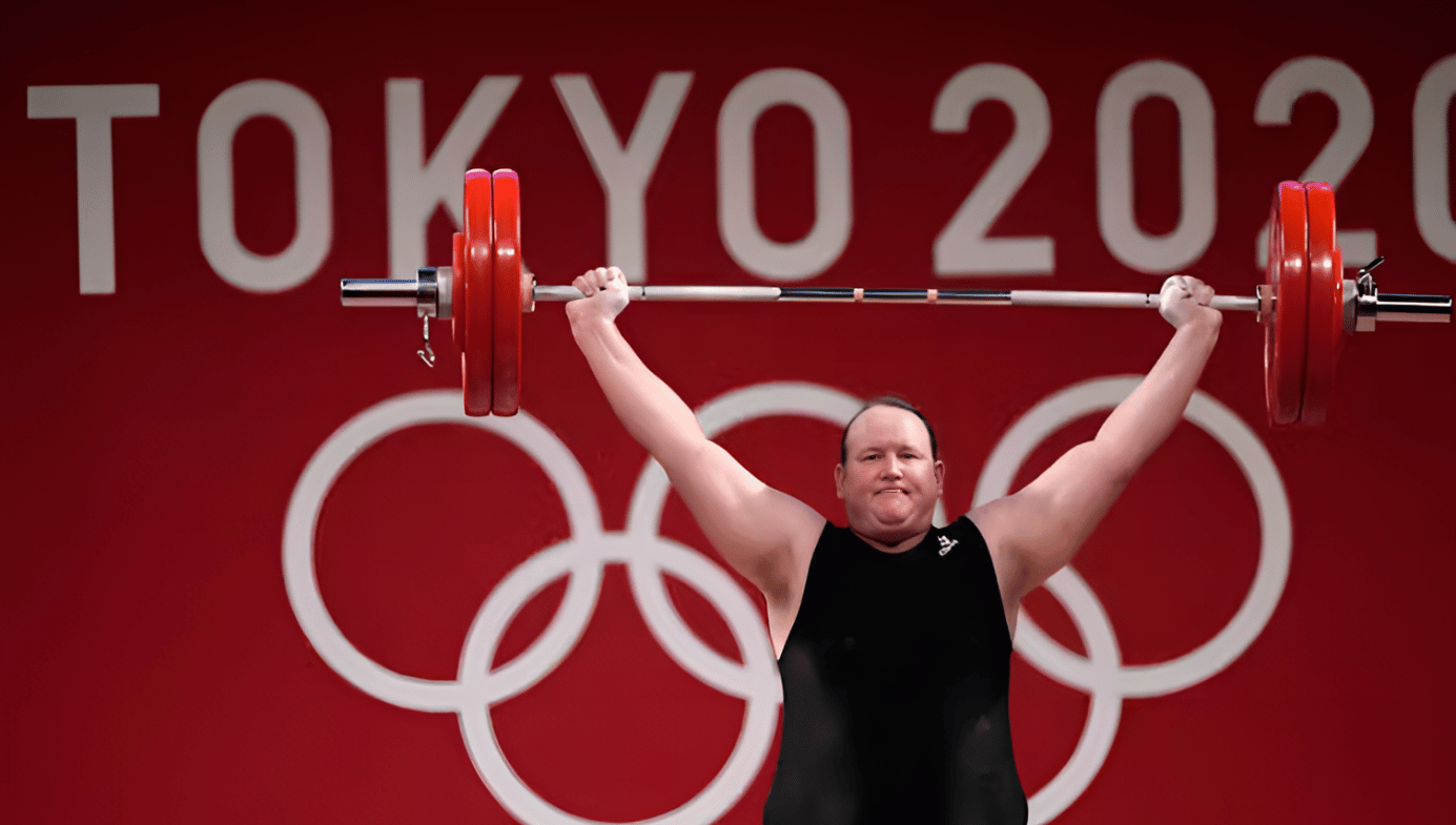 Athlete holds up barbells in front of a "Tokyo 2020" Olympic sign.