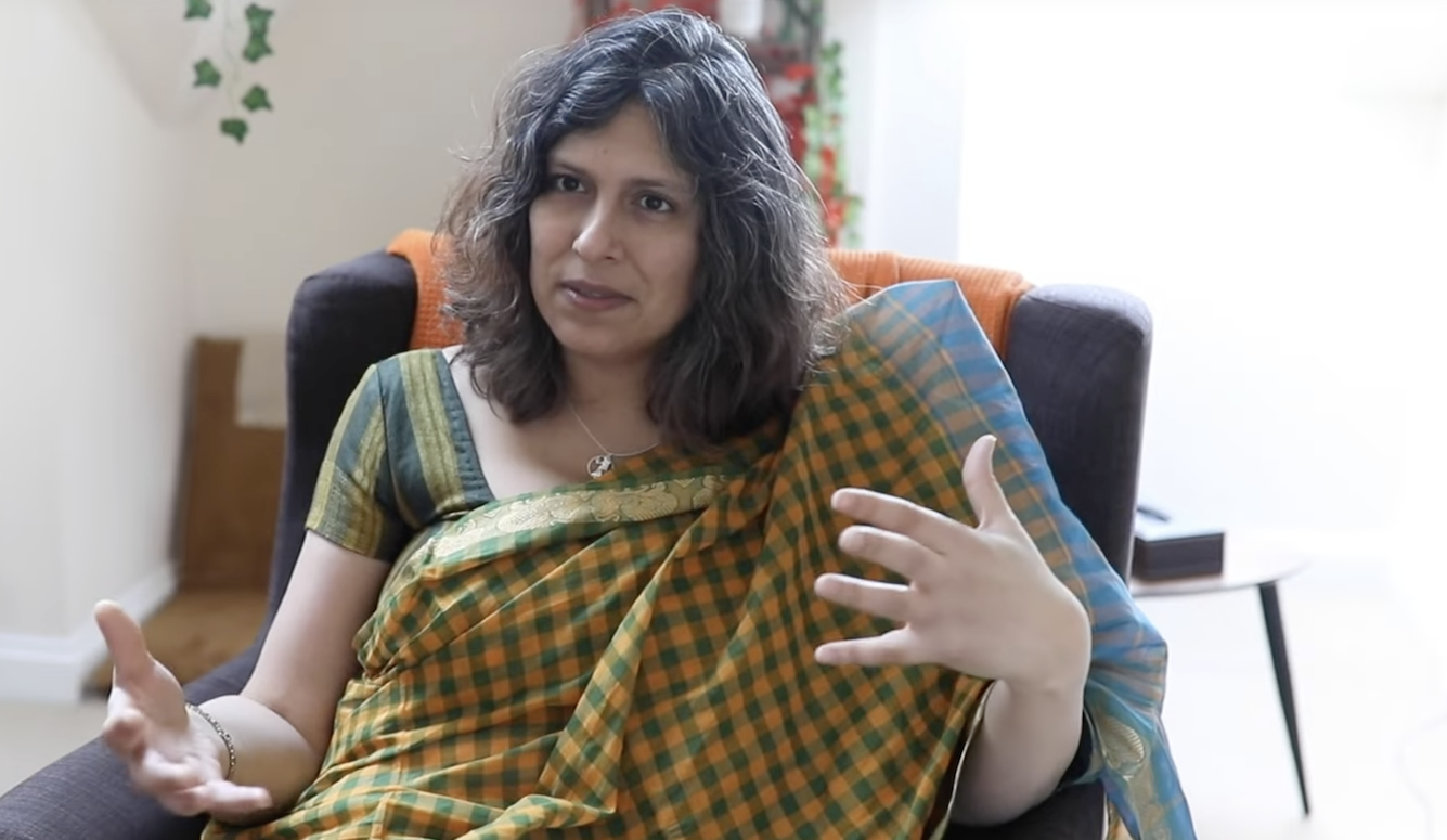 Image of Mridul Wadhwa in a checked sari, sitting in a chair. 