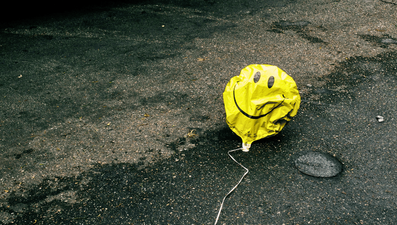 A deflated yellow smiley face balloon on a dirty road.