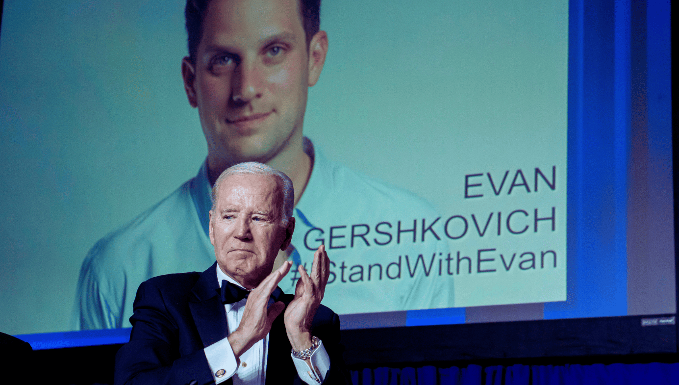 United States President Joe Biden applauds while standing in front of a sign calling for the release of Evan Gershkovich 