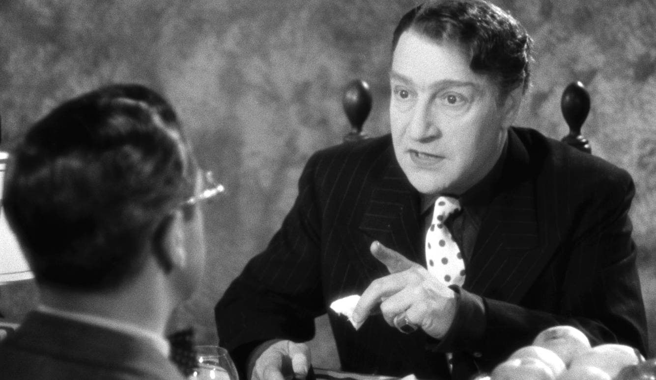 Sacha Guitry as Jean Lécuyer in Ils étaient neuf célibataires (1939), seated at a table,  with a polka dot tie