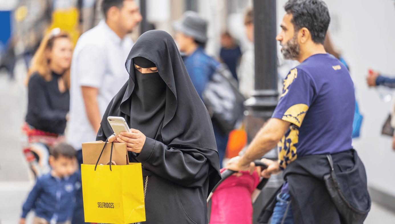 A Muslim woman in London wearing a niqab, using a mobile phone while shopping on Oxford Street.