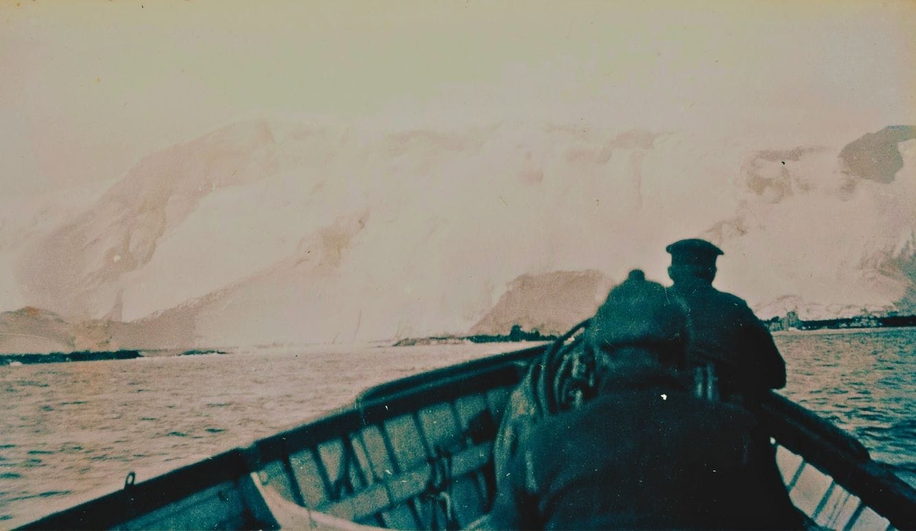 Old photo of explorers on a boat in Antarctica in front of an iceberg.