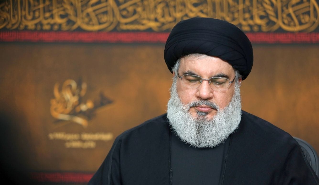 Sayyed Hassan Nasrallah, dressed in black with a black headcovering and grey beard. 