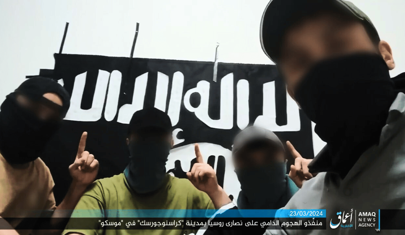 Jihadis with blurred faces and masks holding up one finger in front of the ISIS flag.