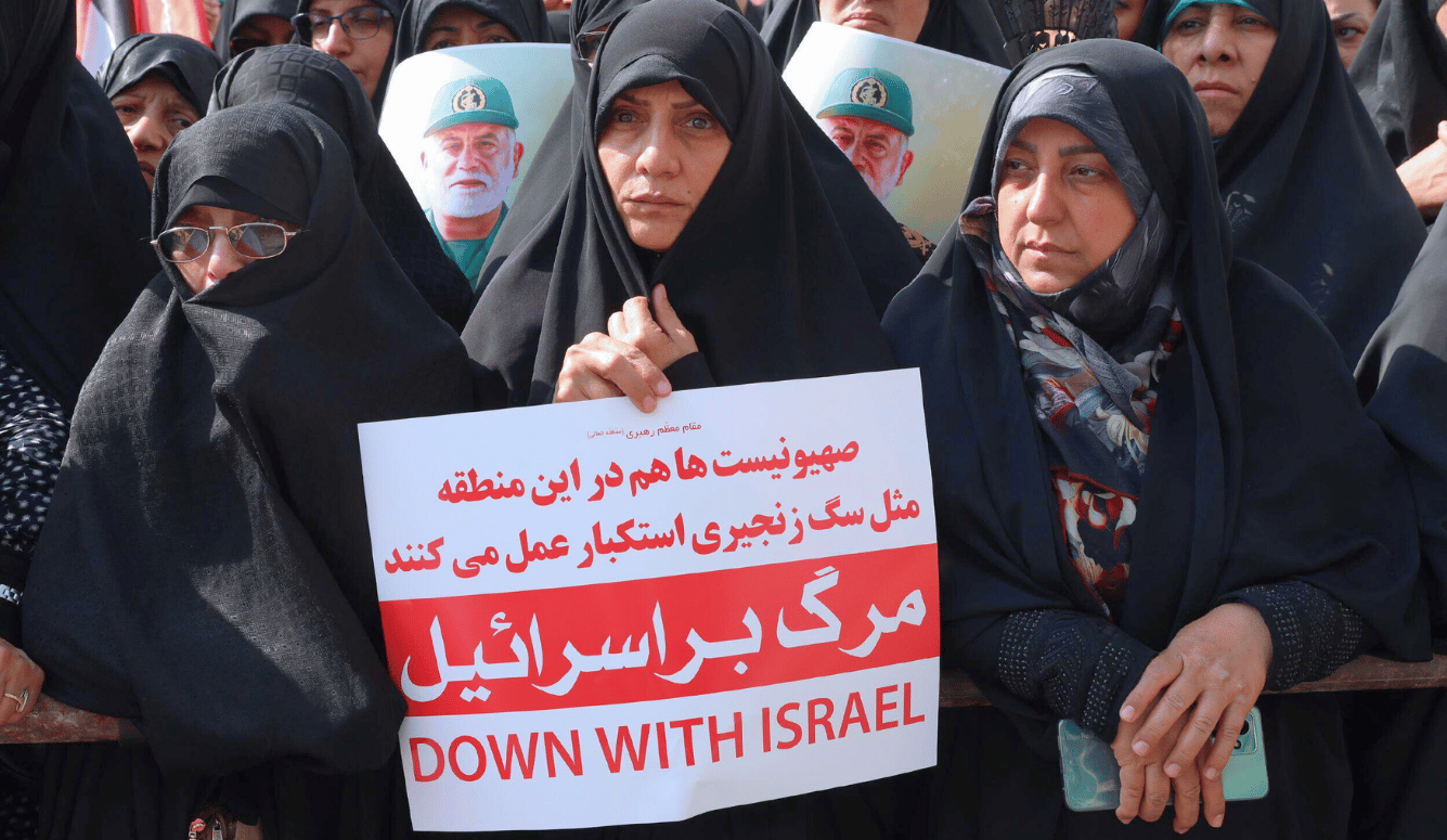 Women in black chadors. The figure in the centre holds a banner reading “Down with Israel.”