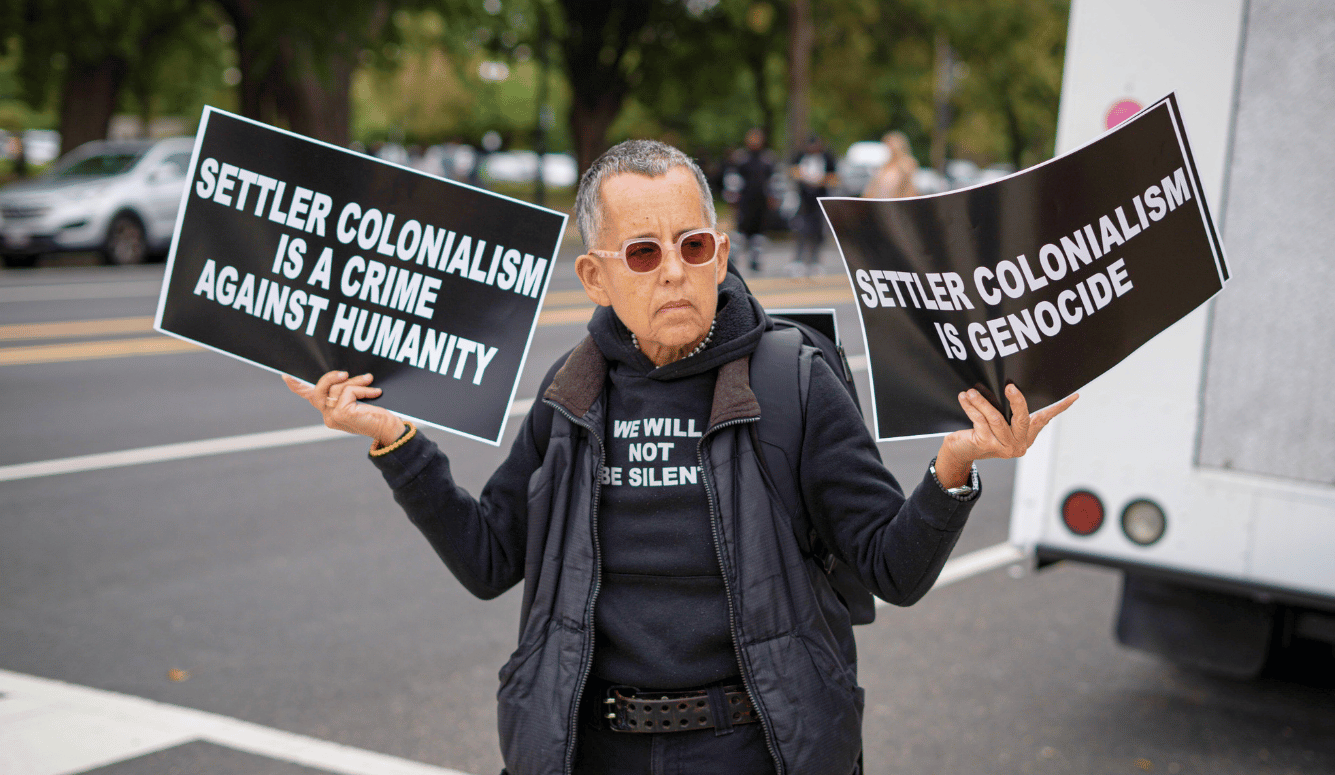 A protester holds up two signs condemning settler colonialism 