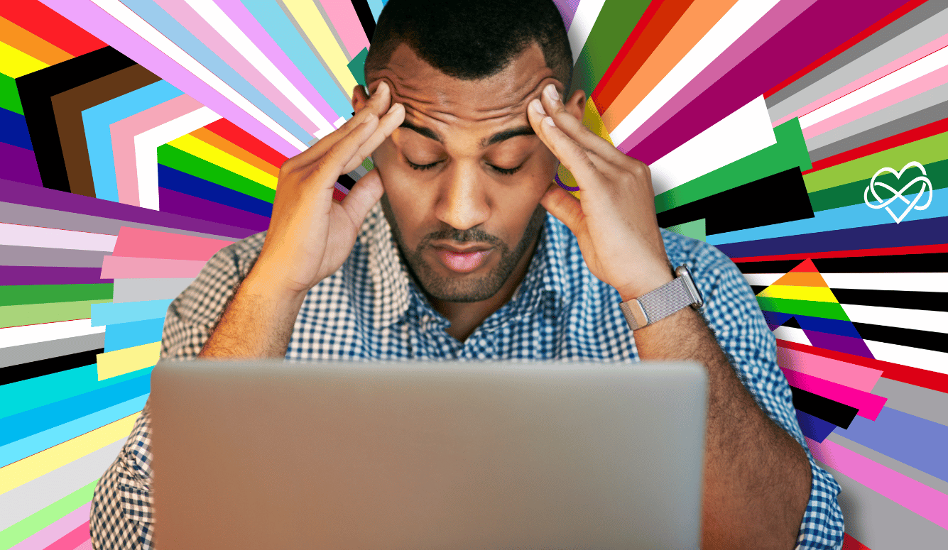 A stressed man rubs his temples in front of his laptop. The background is different pride flags. 