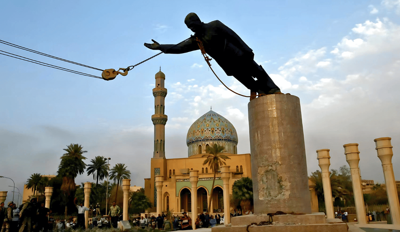 US Marines topple the statue of Saddam Hussein in Baghdad's Firdos Square w.  mosque in the background.