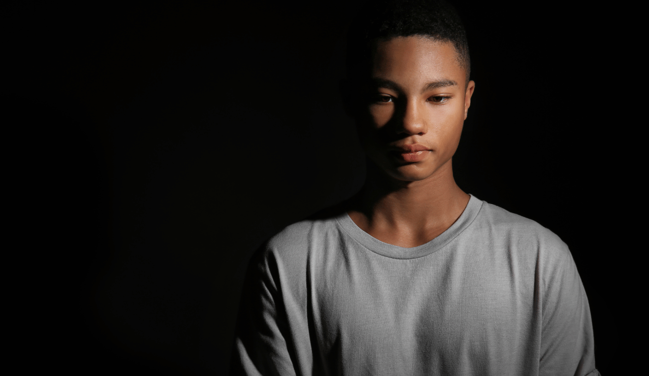 A sad-looking teen boy with light brown skin, of African American appearance.