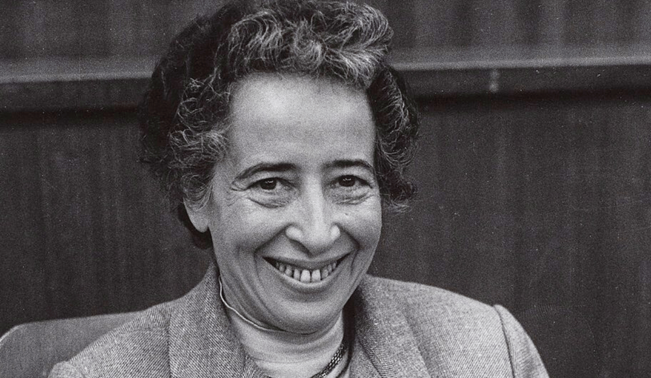 Hannah Arendt in a black and white portrait. She has a beaming smile and is around 50 years old.