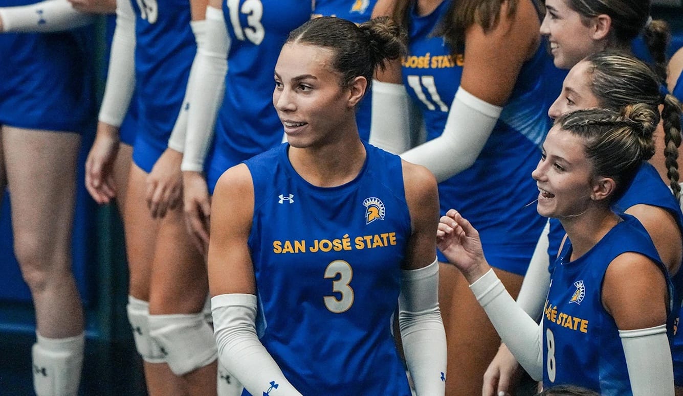 Volleyball players. In the centre, a tall, masculine looking person in San José team kit. 