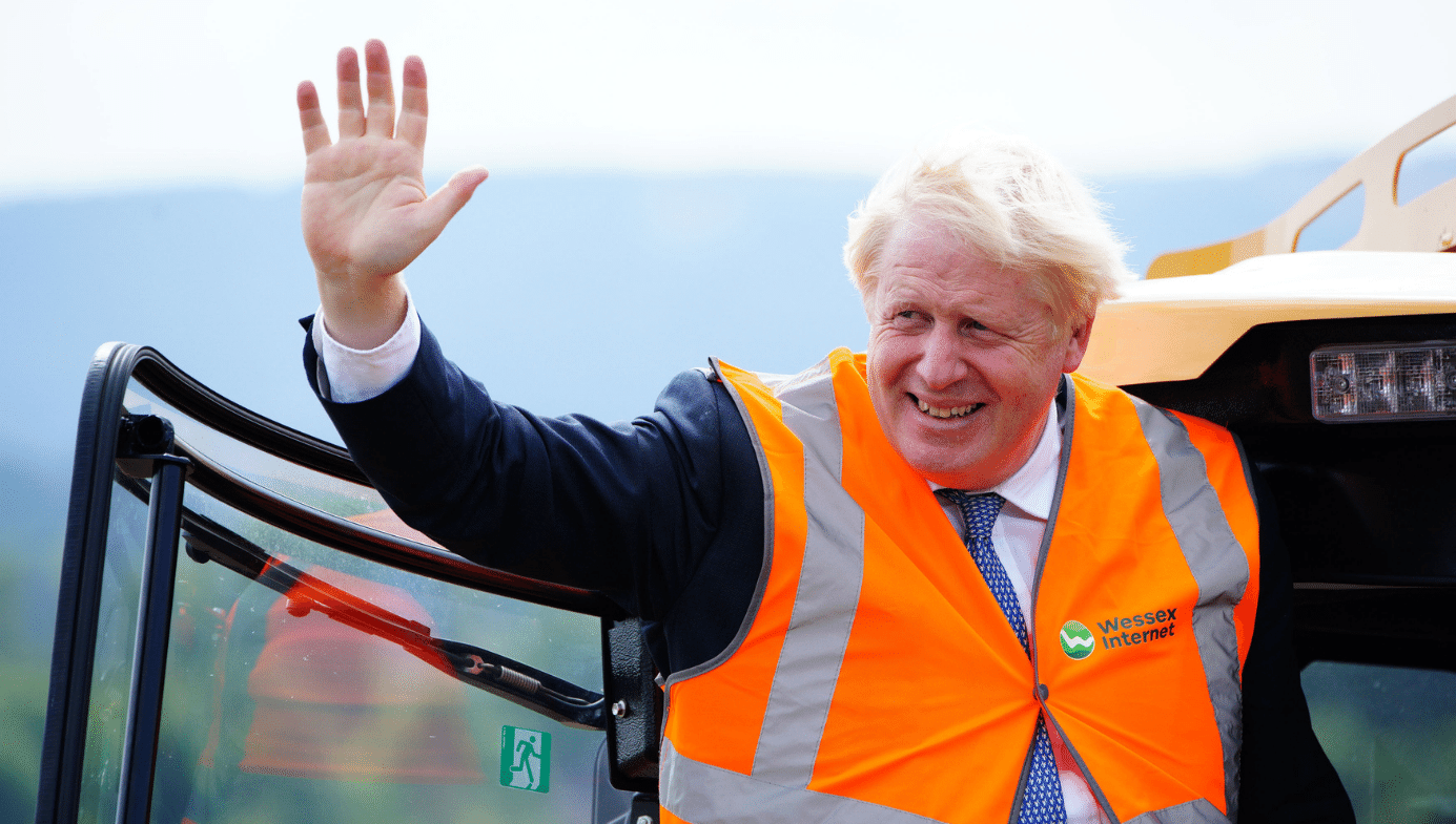 Boris Johnson waves. He wears a hi-vis orange vest.