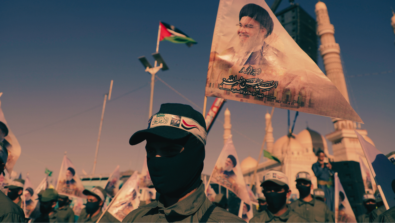 Houthi follower at a march, with blak mask, headband, pennant showing Ayatollah Khameini