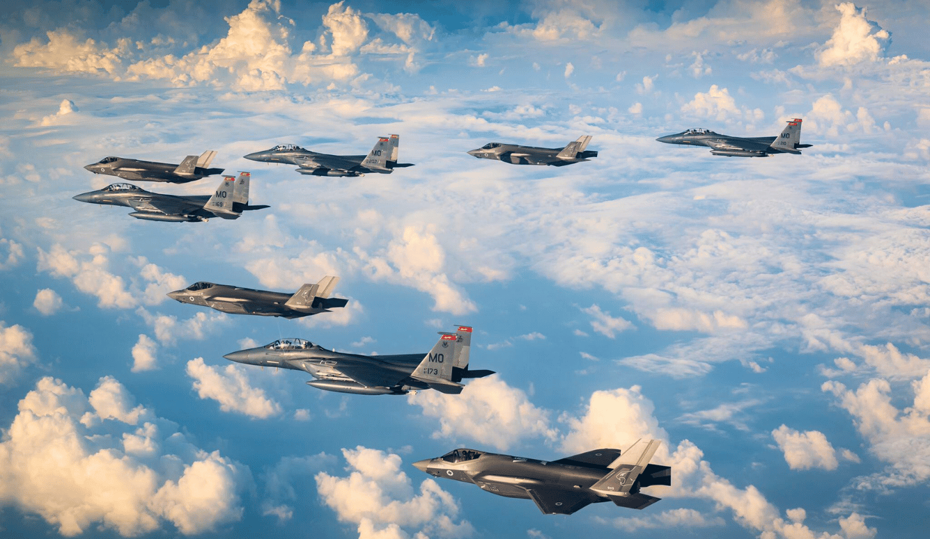 Jet fighters fly in a V shape through the clouds.