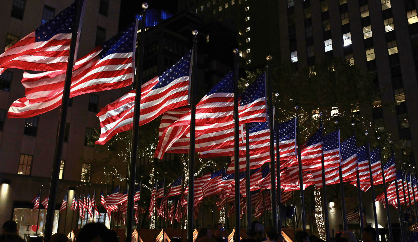 American flags fly in New York, at night. They are lit up. 