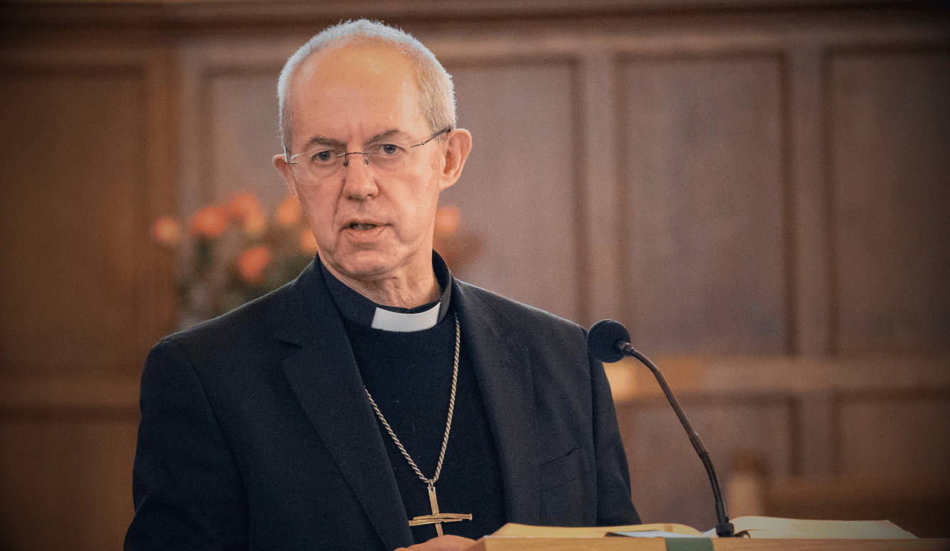 Justin Welby is a white man in his 60s with glasses in the robes of an archbishop with a large cross around his neck.