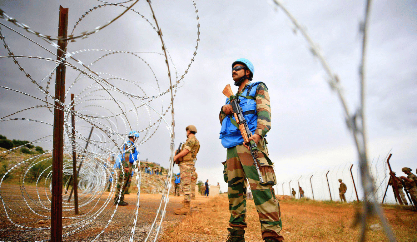 UNIFIL soldiers with gun behind barbed wire.