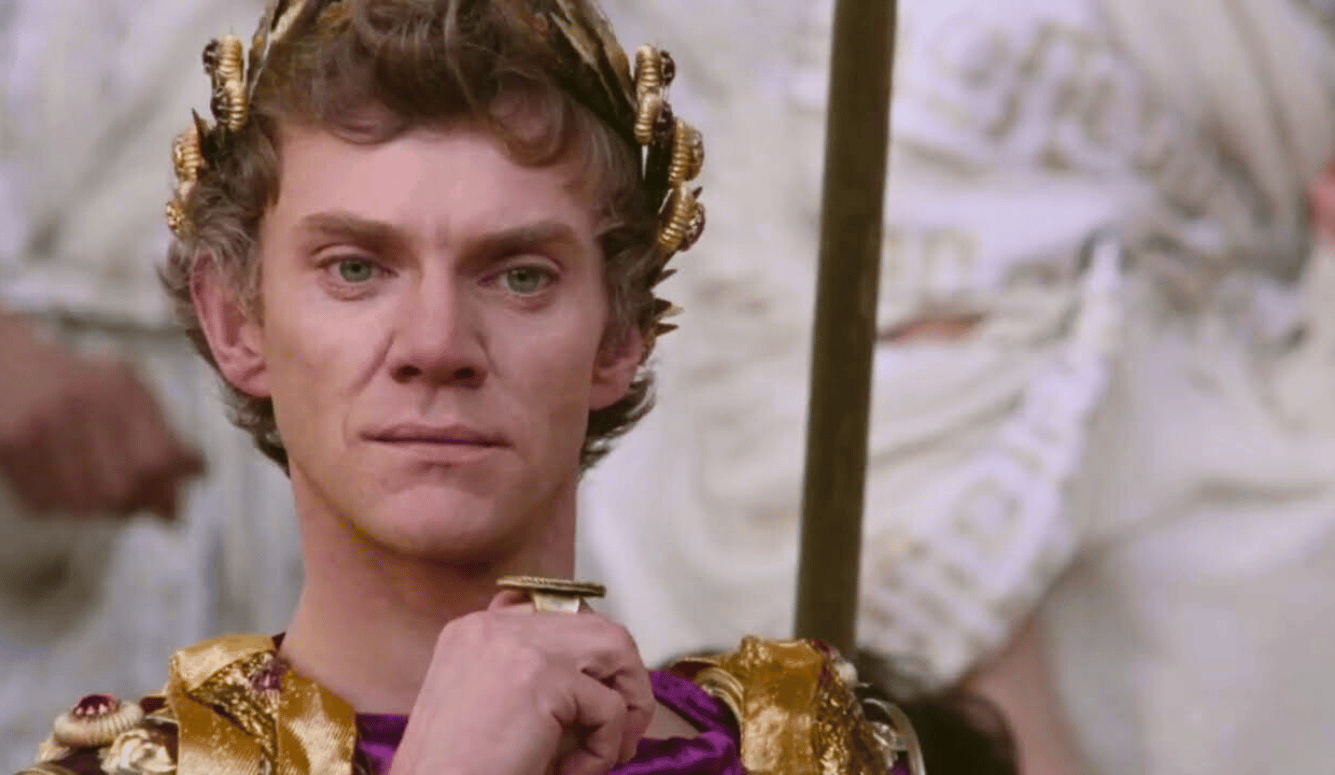 An actor in Roman costume with a gold crown. He is a man in his 50s, blonde hair, blue eyes wearing purple and gold.