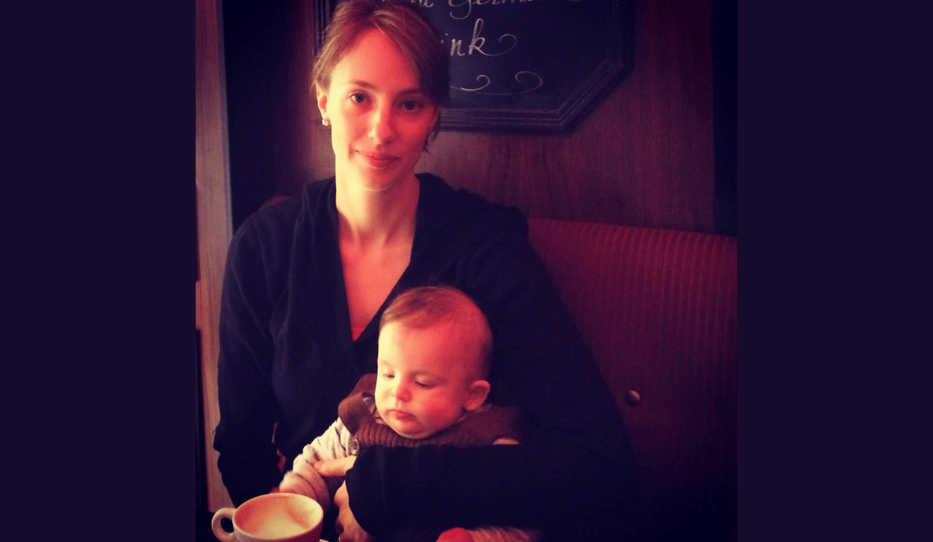 The author is a pale-skinned woman in her twenties. She holds a male infant. There is a coffee up in front of her. 