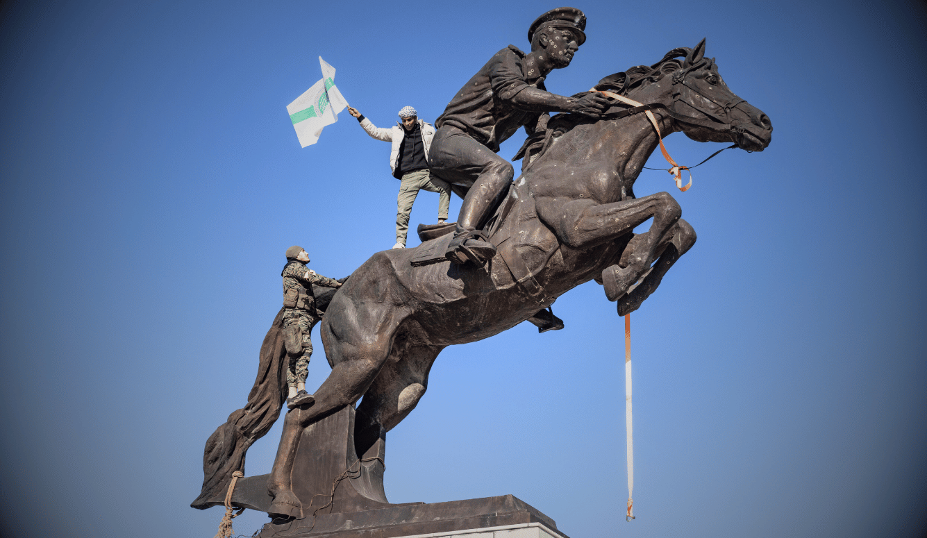 A statue of a horse with a man riding it is climbed by rebels flying a white and green flag. 