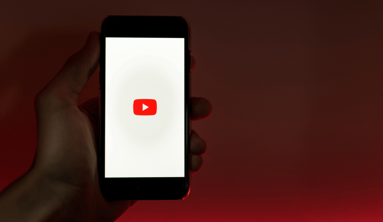 A hand holds a phone displaying the YouTube logo. 