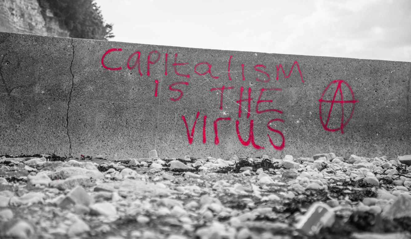 A graffitied wall which says CAPITALISM IS THE VIRUS. 