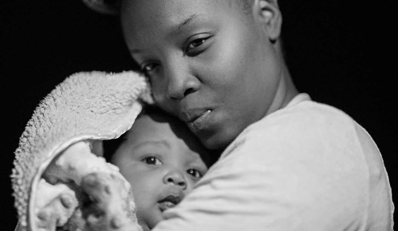 A young mother holding her baby. Both have dark skin. 