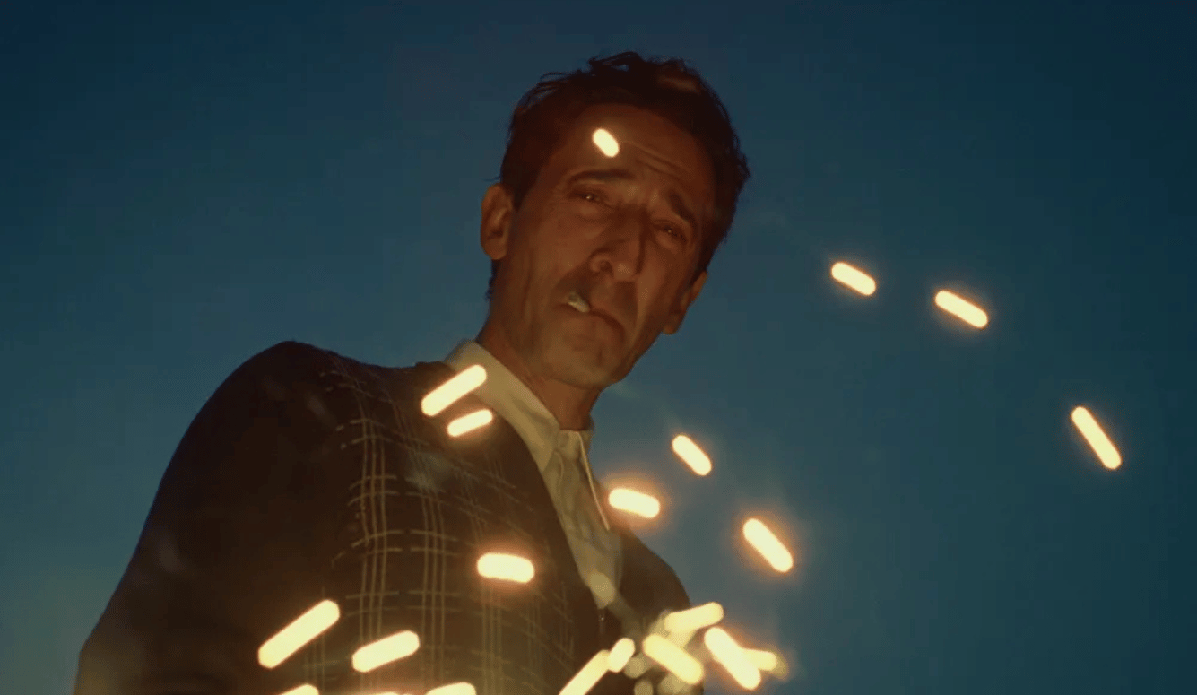 Adrien Brody as architect László Tóth is looking down at the camera, smoking, surrounded by sparks.