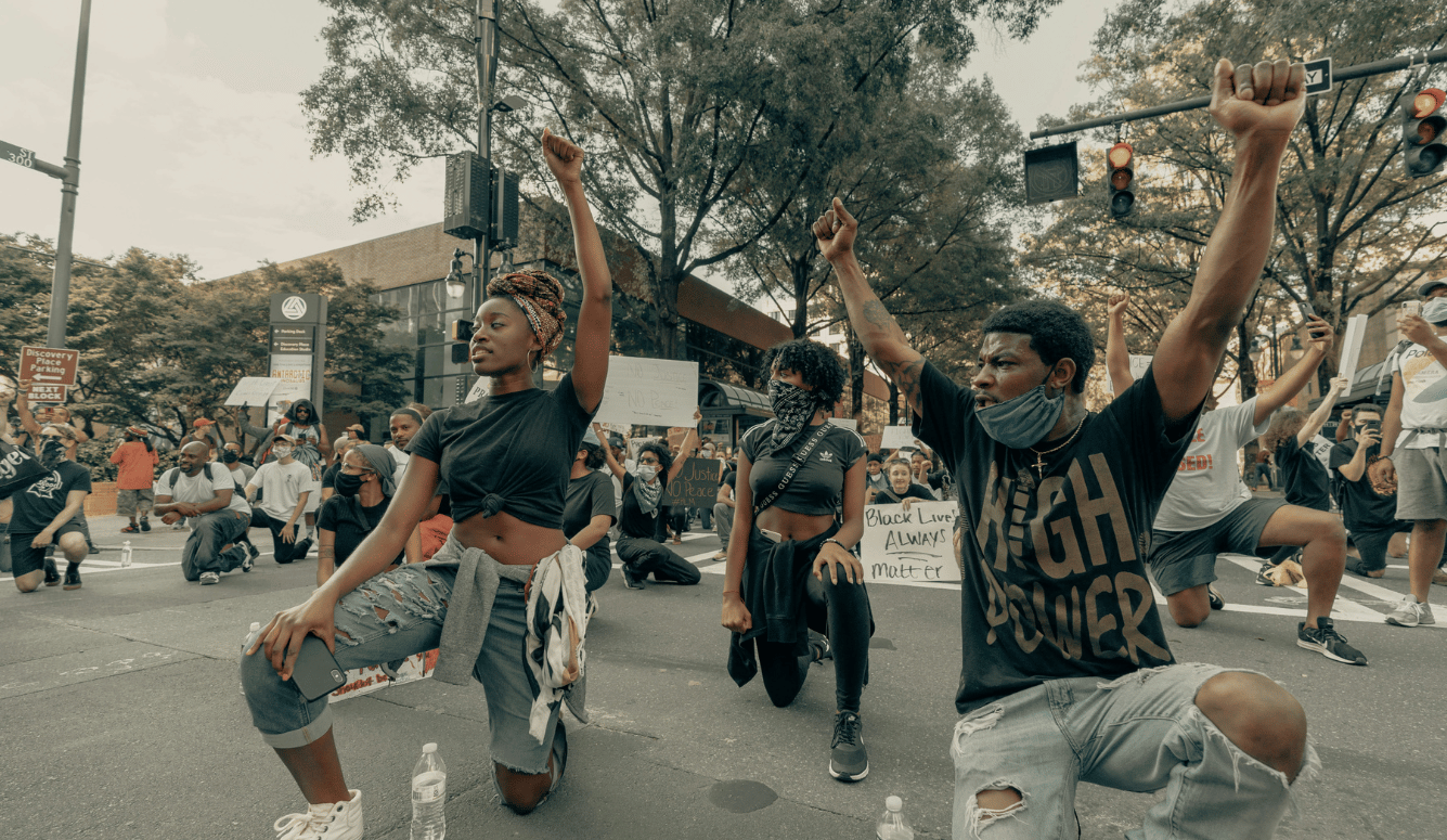 3 young black people raise fists at a BLM protest.