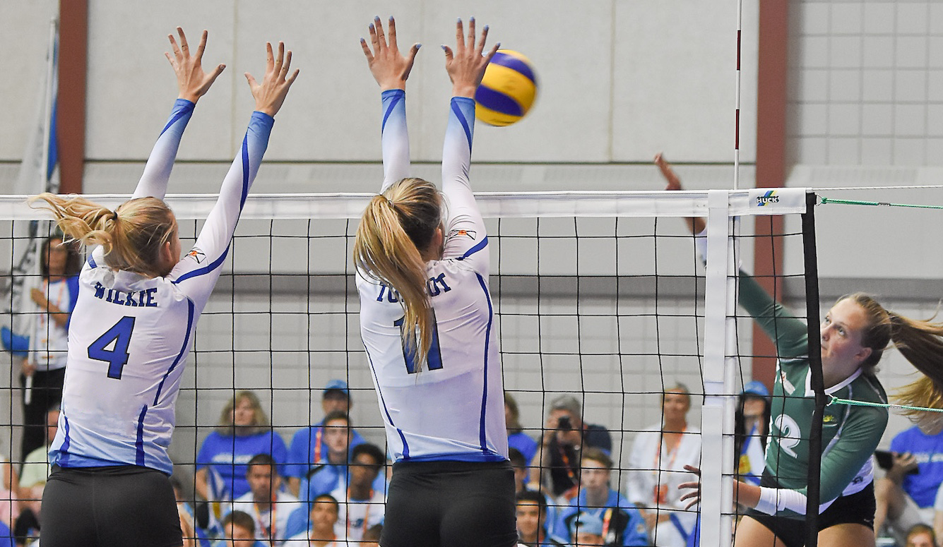 Female volleyball players at the net. Spectators in the background. 