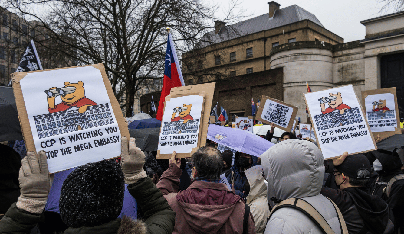 Protestors carry signs reading “CCP is watching you. Stop the mega embassy.”